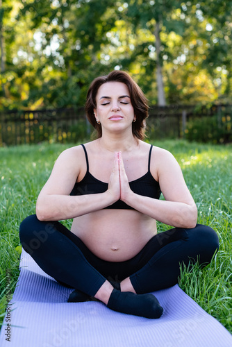 Pregnant woman doing yoga and meditating on grass in the yard, deep breath with fresh air do yoga lotus pose. Yoga Motherhood, mental health, and Pregnant Concept