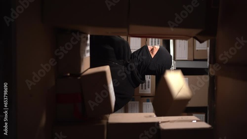 Stealthy criminal wearing black balaclava sneaking into warehouse at night photo