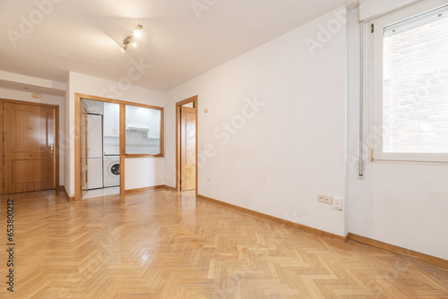 An empty living room in an apartment with a kitchen with a serving hatch window and French oak parquet floors laid in a herringbone pattern