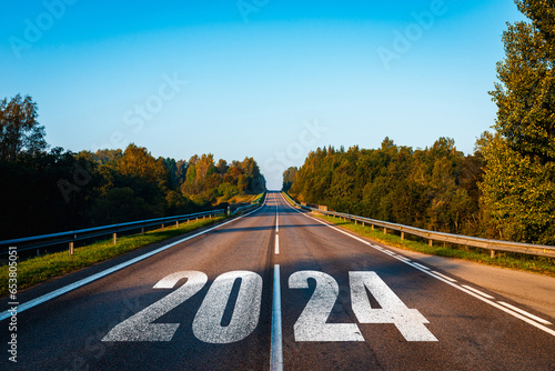 Asphalt road with 2024 text goes to horizon. Sunshine on horizon and the road straight forward. Moving forward into new year concept. Clear and positive perspectives ahead.Early autumn morning.