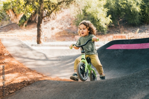happy little boy skater style training with his bike on pump track circuit
