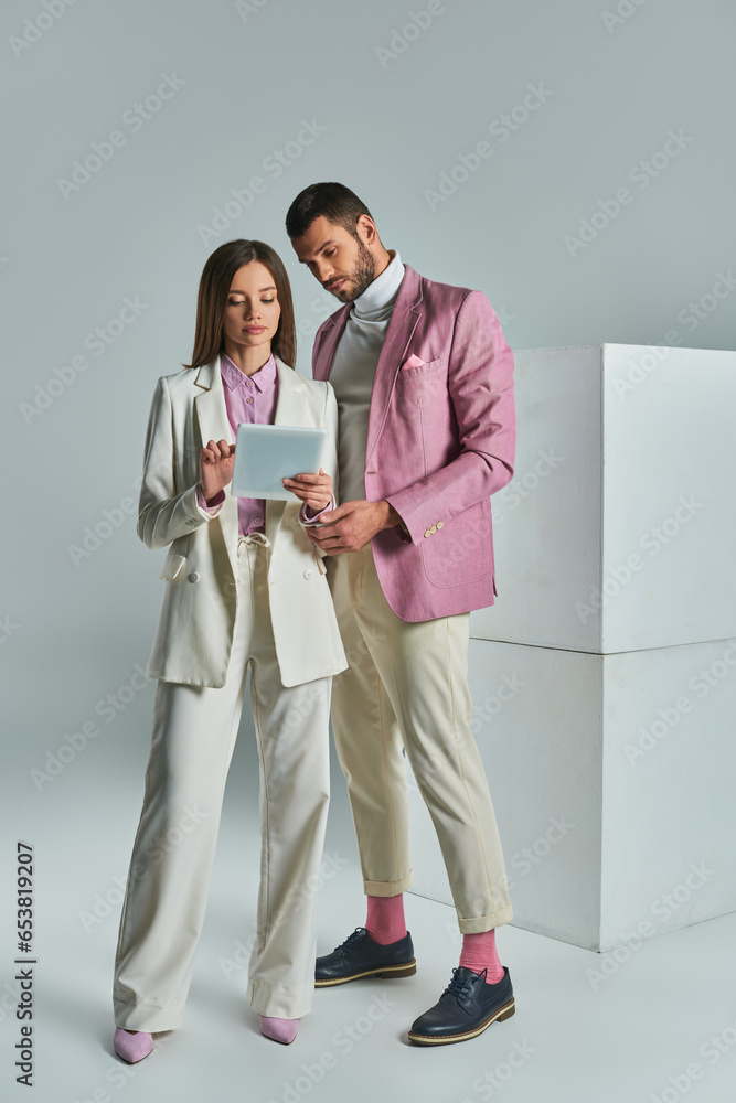 young business couple in stylish formal attire looking at digital tablet near white cubes on grey young business couple in stylish formal attire looking at digital tablet near white cubes on grey