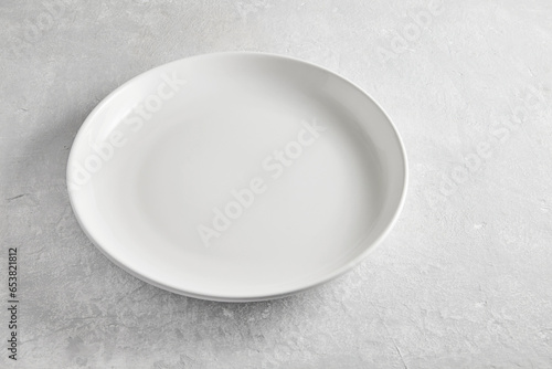 Empty white ceramic plate on gray concrete table high angle view. Template for food display and restaurant menu layout