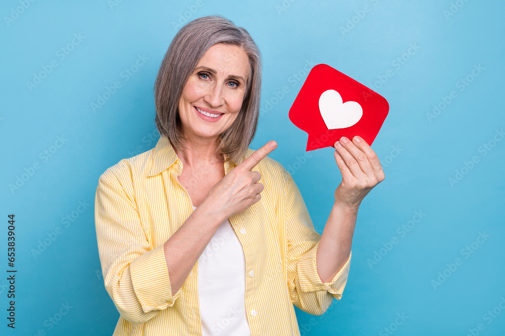 Photo of shiny cheerful woman dressed yellow shirt pointing finger heart like card isolated blue color background Photo of shiny cheerful woman dressed yellow shirt pointing finger heart like card isolated blue color background