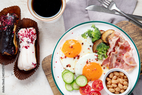 Traditional Englis breakfast plate with bacon strips, sunny side up eggs, vegetables and cake on light background photo