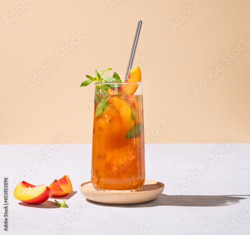 Refreshing peach ice and mint tea. Vegan homemade cold summer drink on tall glass on a light background with fresh fruits and shadows.