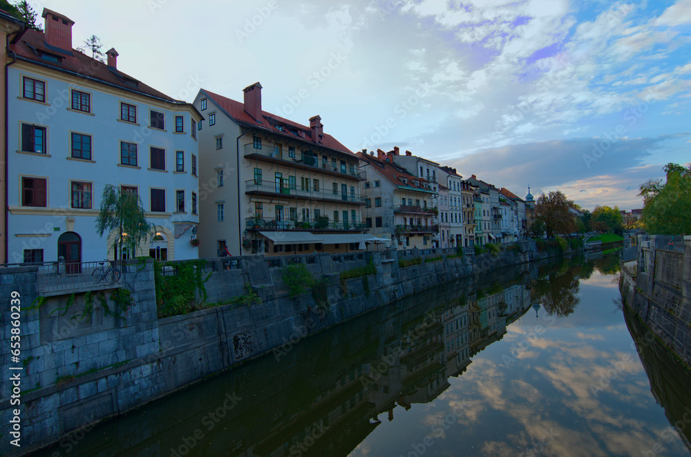 Scenic landscape view of Ljubljana. Embankment of Ljubljanica River with ancient colorful buildings against blue sky. Typical architecture of Ljubljana downtown. Travel and tourism concept