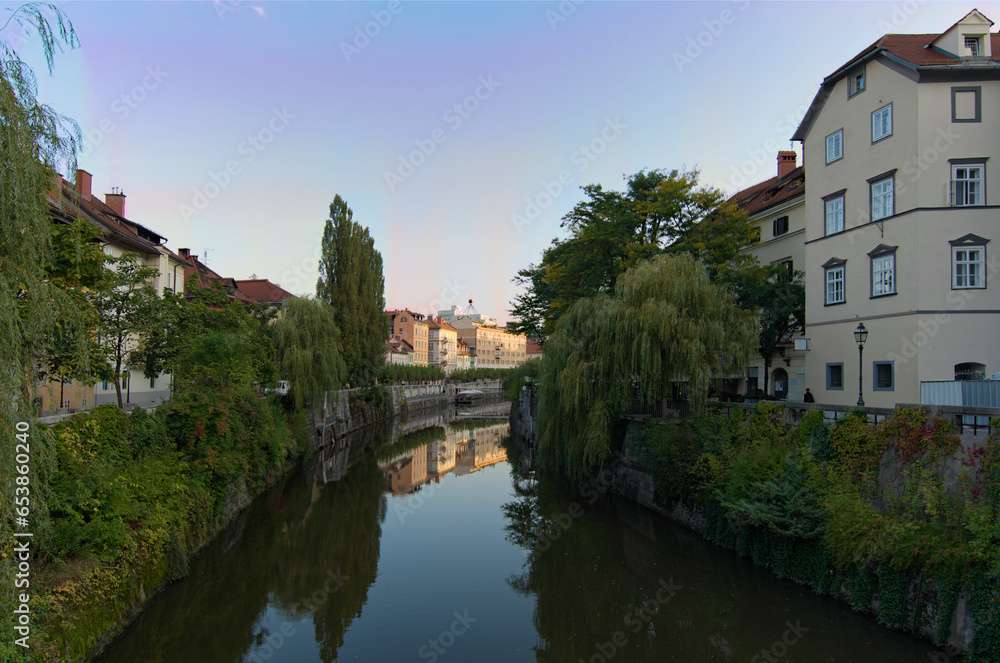 Picturesque cityscape view of Ljubljana. Embankment of Ljubljanica River with ancient colorful buildings against blue sky. Typical architecture of Ljubljana downtown. Travel and tourism concept