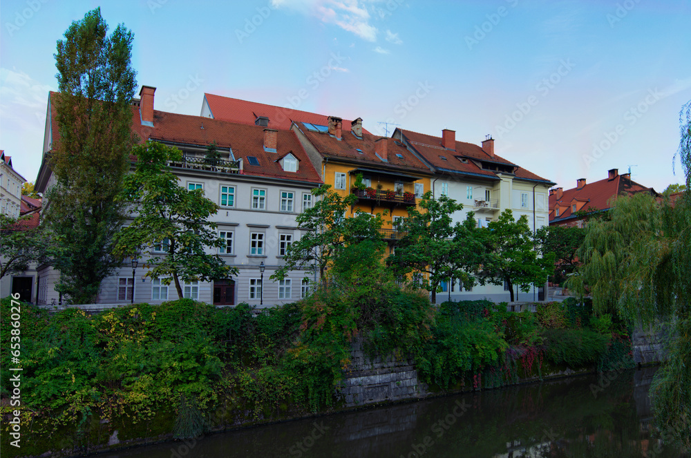 Picturesque cityscape view of Ljubljana. Embankment of Ljubljanica River with ancient colorful buildings against blue sky. Typical architecture of Ljubljana downtown. Travel and tourism concept