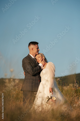 groom holding his beautiful bride in his hands, photo shoot in the middle of nature, sunny day in the meadow, love between two people, groom and bride, newlyweds smile and love