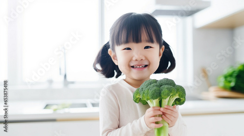 Little beautiful asian girl posing with broccoli in the kitchen. Healthy vegan baby foods concept.