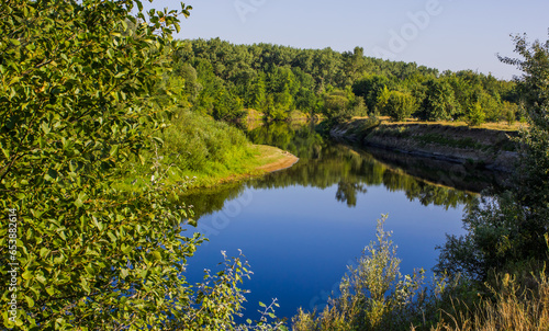 a small river with a winding bed, with a steep bank, grass and trees on the bank during the day in Ukraine in Europe