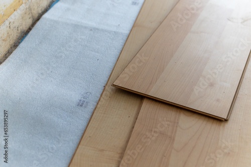 A close up portrait of stacked imitation wood laminate floorboards lying on some sound isolation ready to be installed to create a wooden floor in a house on a screed floor.