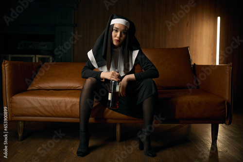 Young sexy nun drinking whiskey from bottle at home