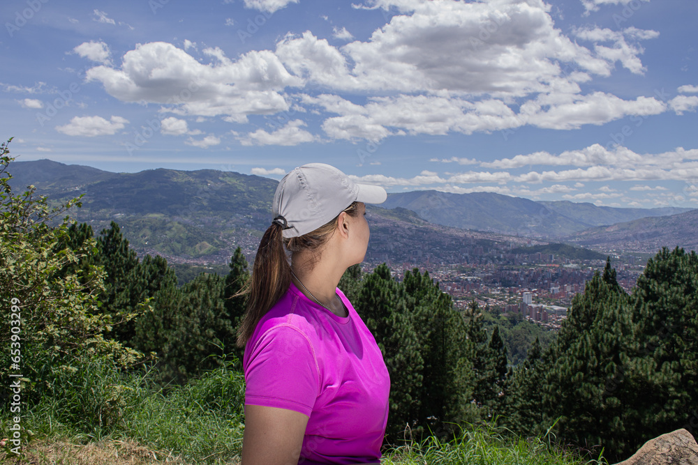 Young woman on top of  mountain looking the city and enjoying nature around.
