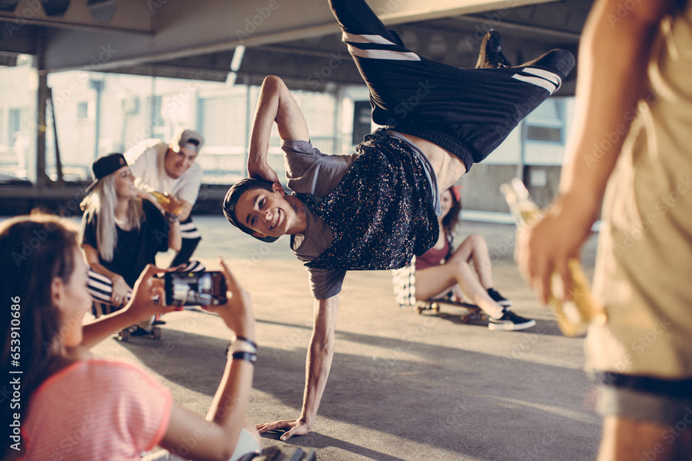 Young and diverse group of people breakdancing and filming it on a smartphone in a parking lot - obrazy, fototapety, plakaty 