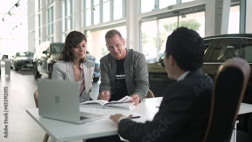 Middle aged couple discussing details of a vehicle they desire with a salesmen at the car dealership