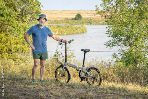 athletic senior man with a folding bike on a shore of the Dismal River in Whitetail Campground in Nebraska National Forest