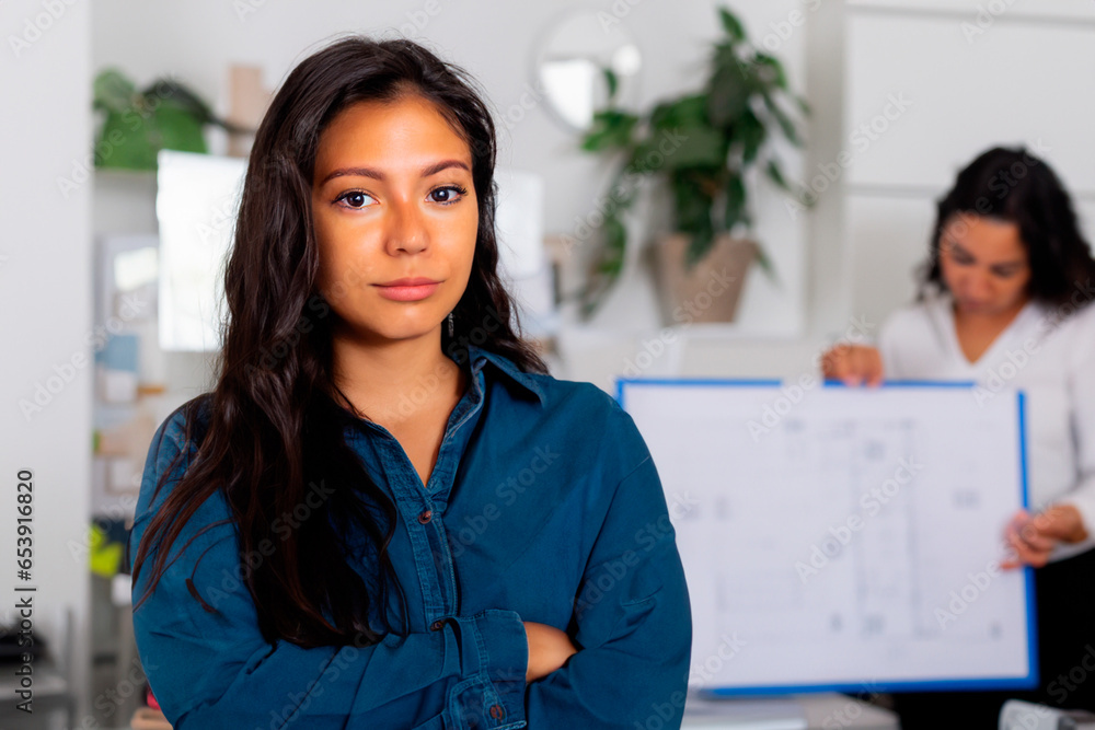 Young woman in blue denim shirt with long black hair stands in office Young woman in blue denim shirt with long black hair stands in office