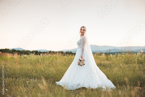 a shot of a beautiful bride in a white lace dress holding a bouquet of dried flowers in the middle of a field, a beautiful blonde, a happy bride in the middle of a wedding photo shoot, love, wedding 