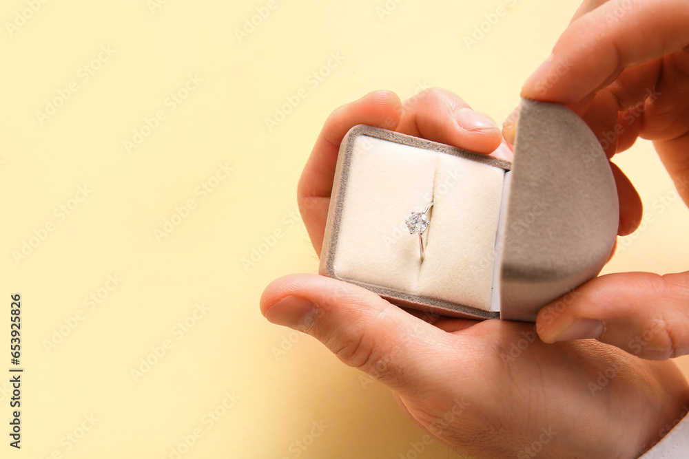 Fototapeta premium Man holding box with engagement ring on beige background, closeup