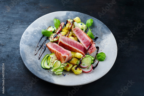 Traditional Italian fried tuna fish steak with gnocchi and cucumber slices served as close-up on a Nordic design plate photo