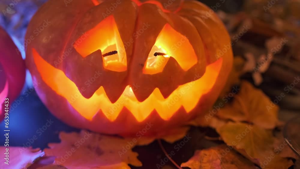 Jack-o-lantern sparkling from inside made from a carved pumpkin on table decorated with autumn attributes for Halloween holiday with flickering lights and burning candles, tracking shot background.