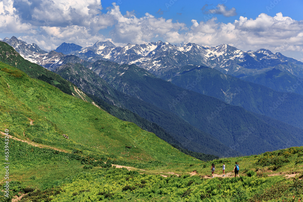 Large, high, green mountains, snow on the peaks, summer, sunny day, tourists walking along the path, Abkhazia, forest.