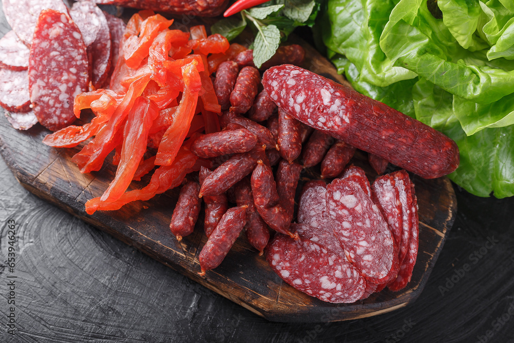 fresh herbs and vegetables, dry-cured sausage, dried pieces of Carpaccio meat, small salami sticks, vintage wooden cutting board, on a black isolated background fresh herbs and vegetables, dry-cured sausage, dried pieces of Carpaccio meat, small salami sticks, vintage wooden cutting board, on a black isolated background