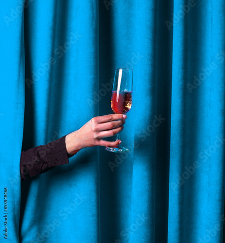 Delicious sparkling wine degustation. Cropped image of female hand holding glass with rose wine over blue background. Concept of alcohol, drink, party, degustation, holiday.