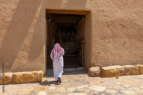 Arab man back view wearing traditional arab clothes wlaking next to Al Masmak Palace Museum in Riyadh Saudi Arabia photo