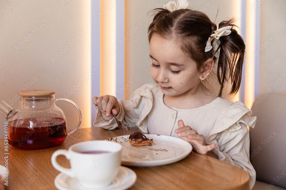 Cute little brunette girl drinking a tea with spoon at the table and eating some cookies. Family weekend. Happy spare time. High quality photo Cute little brunette girl drinking a tea with spoon at the table and eating some cookies. Family weekend. Happy spare time. High quality photo