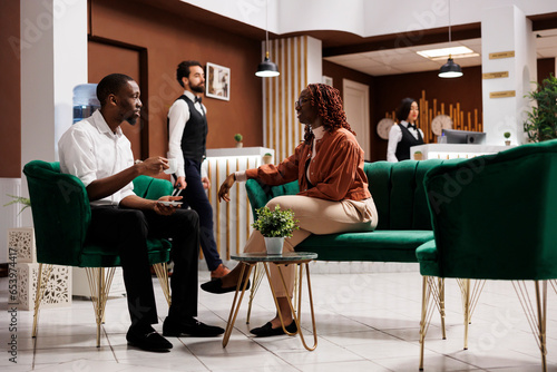 African american people waiting for room check in, sitting in lounge area at luxury hotel. Joyful couple arriving at modern expensive resort, preparing for front desk registration.