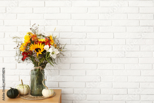 Fototapeta Naklejka Na Ścianę i Meble -  Wooden cabinet with bouquet of autumn flowers and pumpkins near white brick wall