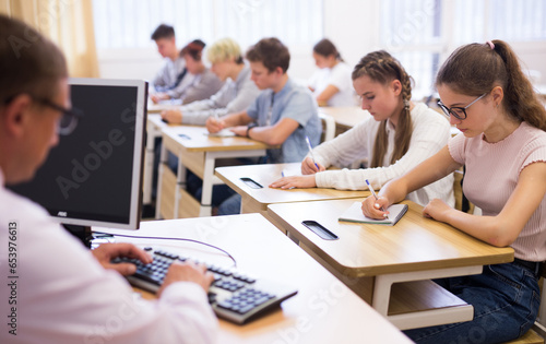 Multiracial group of teenage students working at class, listening explanations of teacher in classroom