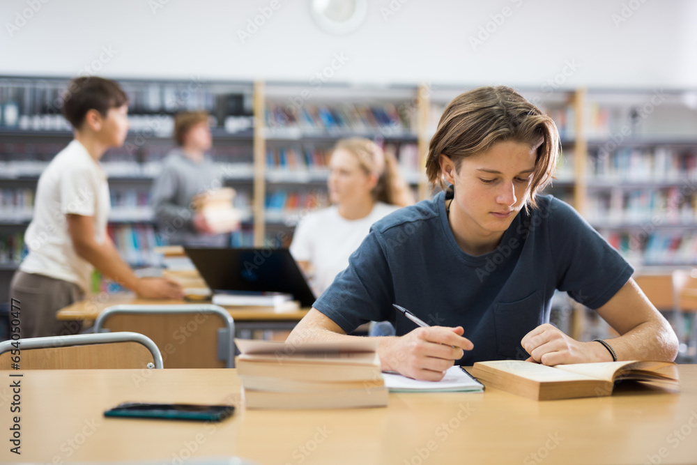 Portrait of teenager reading books and writing in notebooks in the library - obrazy, fototapety, plakaty 