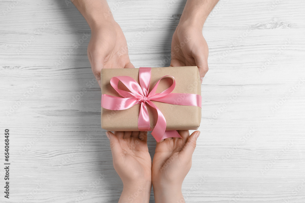 Man giving gift box to woman on white wooden table, top view Man giving gift box to woman on white wooden table, top view