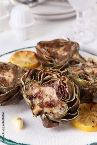 Plate with tasty grilled artichokes on white table, closeup