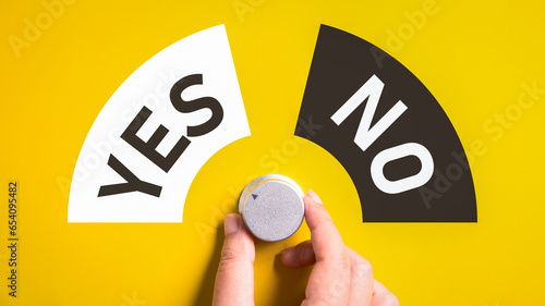 Hand adjusting the volume selector for choosing YES or NO on isolated yellow background. Questionnaire question and answer concept. photo