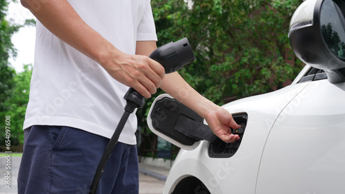 Progressive man install power cable plug to his electric vehicle, EV car from home charging station. Electric car driven by clean and renewable energy to preserve environment. Eco-friendly automobile.