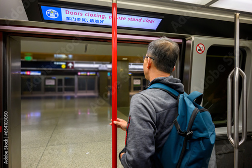 Man standing by the open door of the airport rail link. The neon board overhead with messages in English and Chinese - Doors closing, please stand clear.