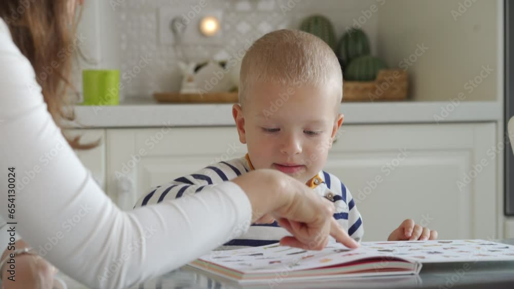mother and toddler child little boy looking at pictures in a book while sitting at the table at home mother and toddler child little boy looking at pictures in a book while sitting at the table at home