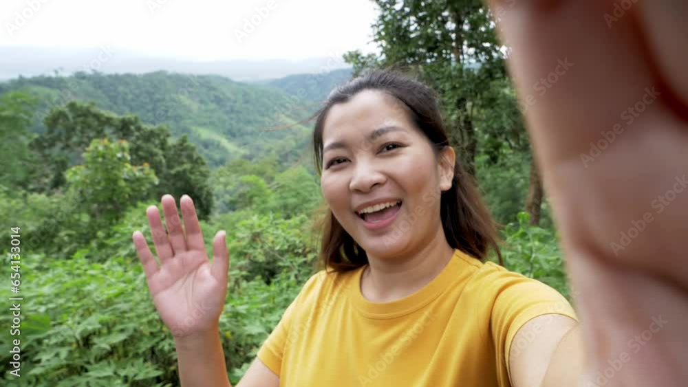 Positive female hipster waving a hand at the camera during video chat online. Smiling hiker gesturing hands. Cheerful traveler exploring nature.