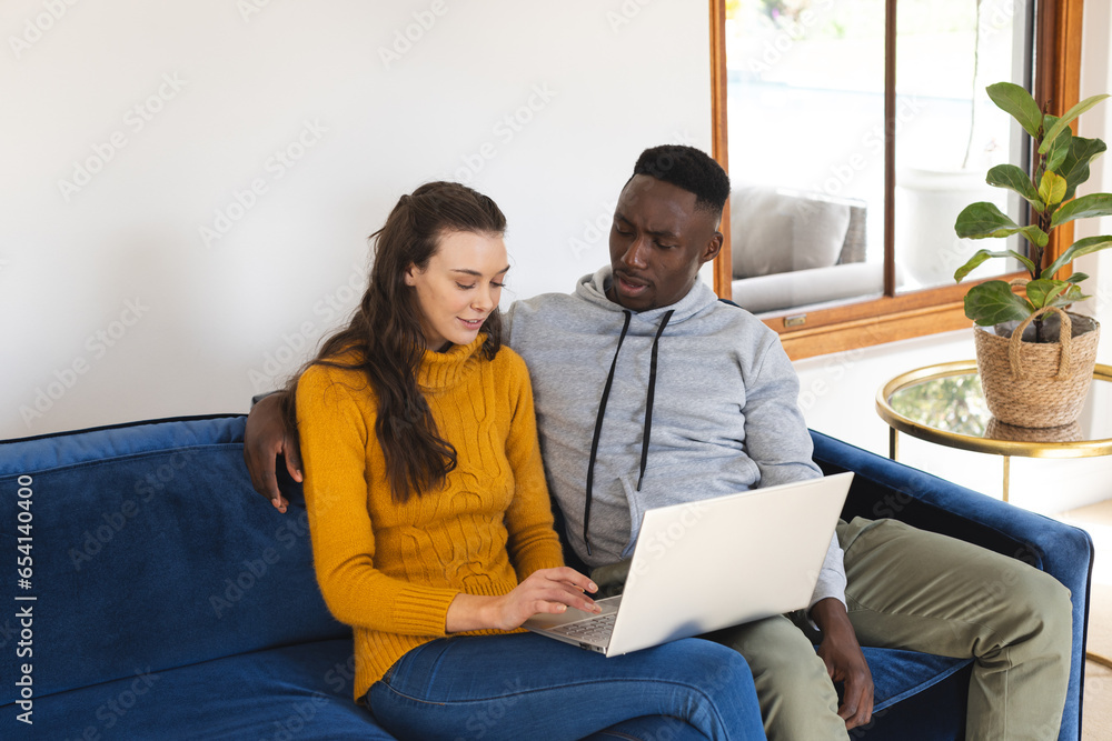 Diverse couple sitting on sofa using laptop at home Diverse couple sitting on sofa using laptop at home