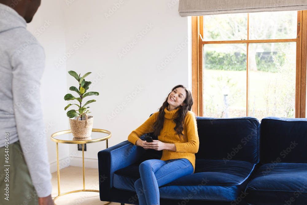 Happy caucasian woman sitting on sofa using smartphone at home