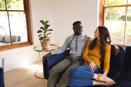 Happy diverse couple sitting on sofa embracing and smiling at home, copy space