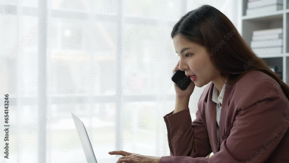 Positive Asian young female accountant using a smartphone at her office desk. Woman relaxing on her mobile application. Positive Asian young female accountant using a smartphone at her office desk. Woman relaxing on her mobile application.