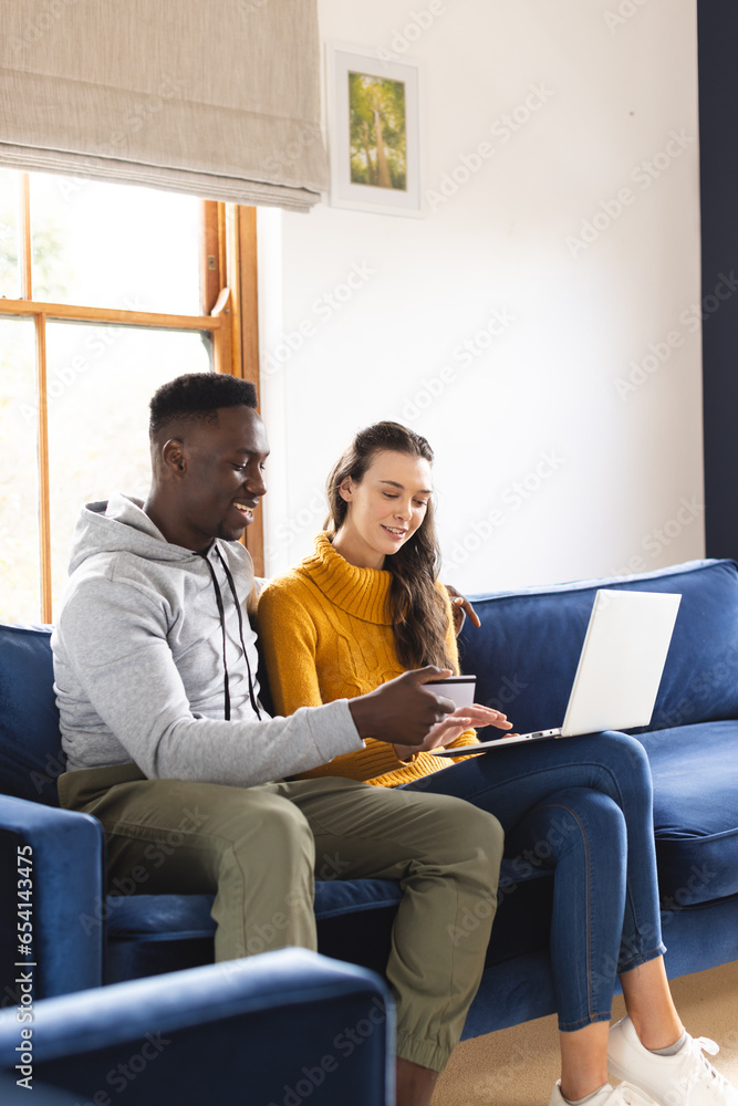 Happy diverse couple sitting on sofa using laptop for online shopping at home Happy diverse couple sitting on sofa using laptop for online shopping at home