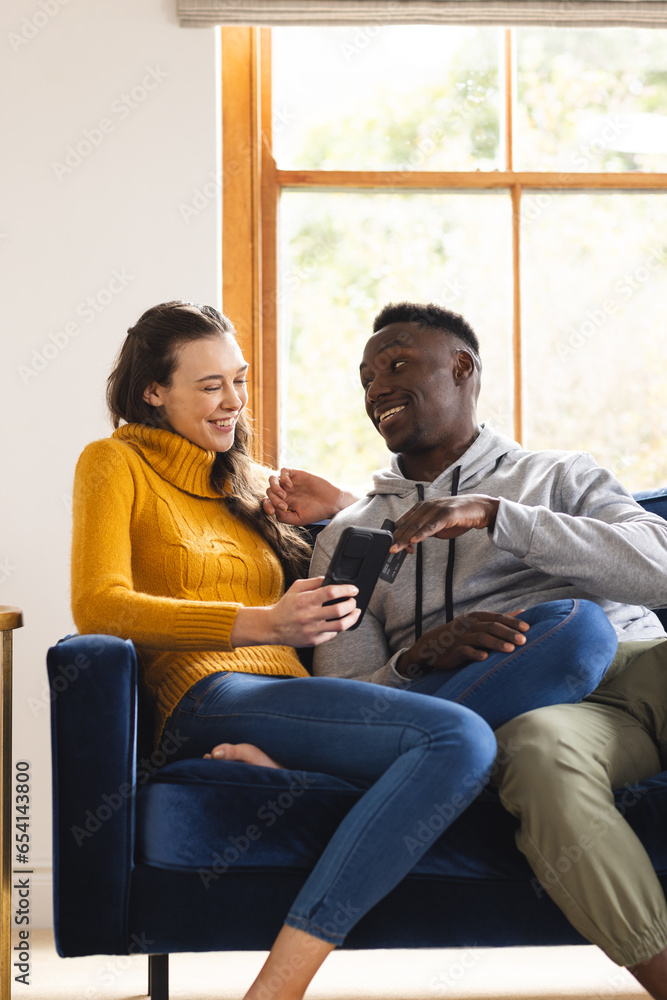Happy diverse couple sitting on sofa using smartphone for online shopping at home Happy diverse couple sitting on sofa using smartphone for online shopping at home