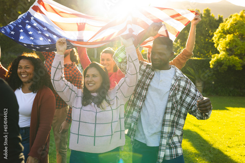 Happy diverse male and female friends holding american flag in sunny garden